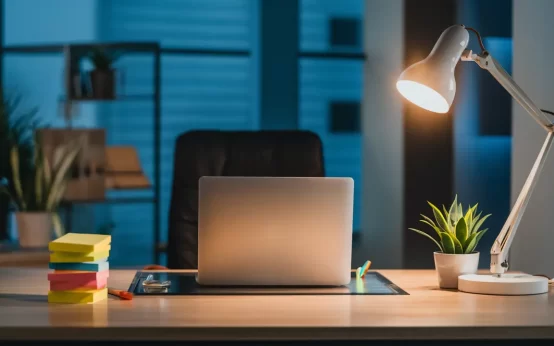Espaço de trabalho moderno com mesa de madeira, laptop, notas adesivas coloridas e planta em vaso.
